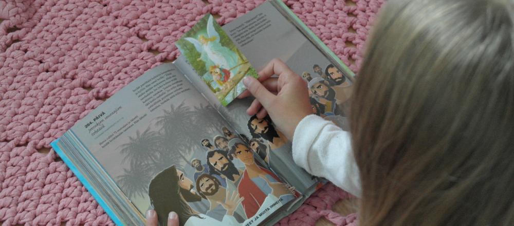 Lapsi lukee lastenraamattua, kädessä suojelusenkeli kuva.